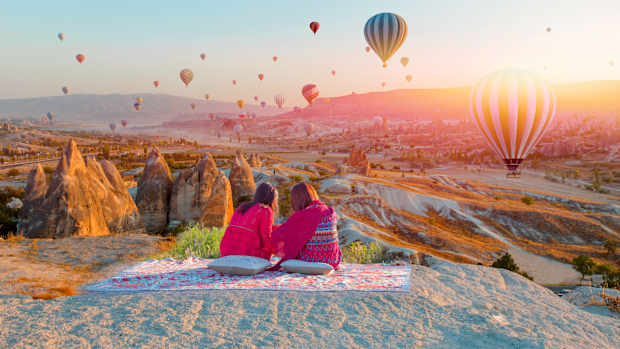 Zwei Mädchen auf einem Hügel beobachten Heißluftballons, die im Abendlicht über Kappadokien fahren