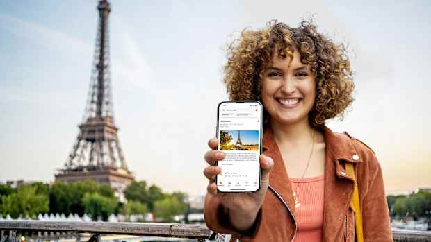 frau zeigt handy mit screen der trips app. im hintergrund sieht man den eiffelturm