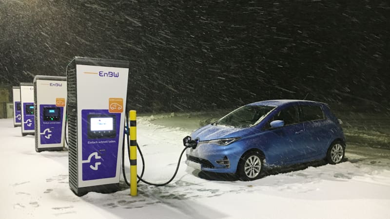 Ein blauer elektronischer Renault Zoe im Winter, bei Schnee und in der Nacht af einem Parkplatzan einer Ladesäule
