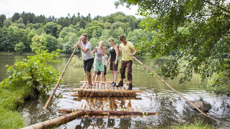 Junge Menschen stehen auf einem Floß aus Baumstämmen auf einem Gewässer