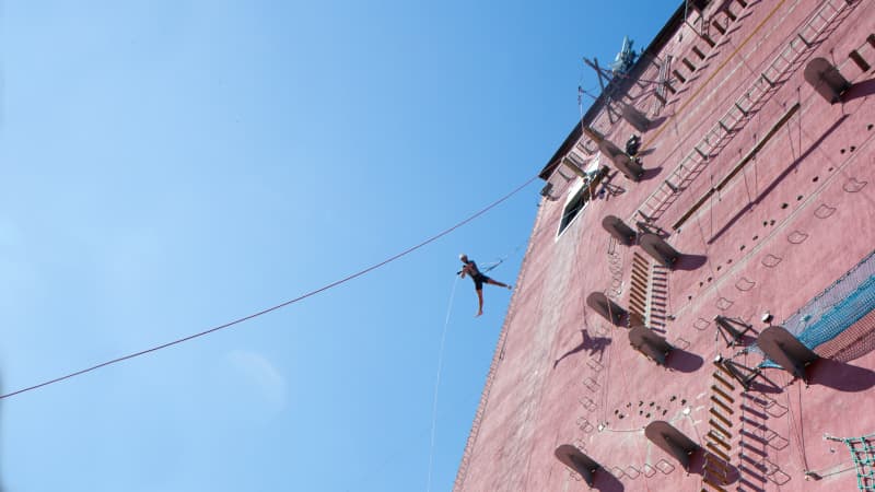 Ein Mensch schwebt gesichert an einem Seil und hängt an einem sehr hohen Gebäude