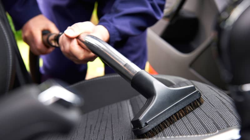 Ein Mann saugt mit einem Bürstenaufsatz einen Autositz