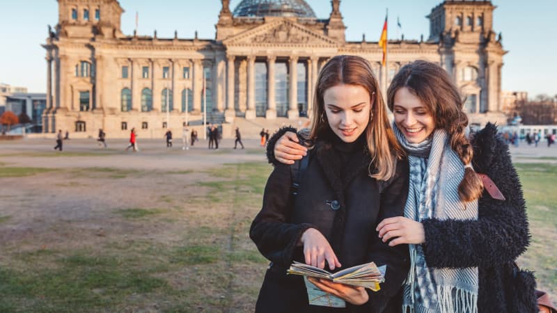 Zwei Frauen stehen vor dem Reichstag in Berlin und schauen auf einen Stadtplan