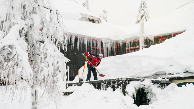 Ein Mann schippt den meterhohen Schnee von dem Dach des Berggasthofes Neues Haus in Oberwiesenthal. Grosse Eiszapfen hängen vom Dach des Hauses.