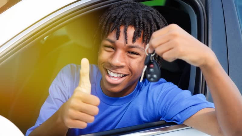 Junger Mann sitzt in Auto mit Autoschlüssel in der Hand