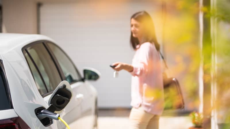Eine Frau mit einem Funkschlüssel steht an einem Elektroauto