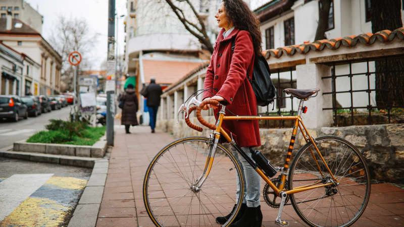 Frau mittleren Alters, die an einem regnerischen Tag in der Innenstadt mit ihrem alten Fahrrad zur Arbeit fährt.