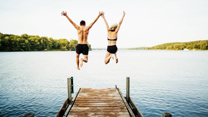 Mann und Frau springen von einem Steg aus in einen See