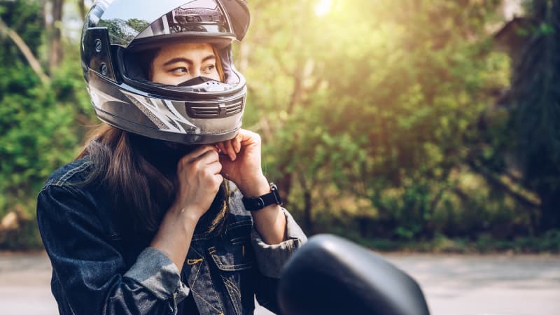 Asiatische Frau, die vor dem Fahren einen Motorradhelm trägt. Helme tragen zur Motorradsicherheit bei, indem sie den Kopf des Fahrers schützen.