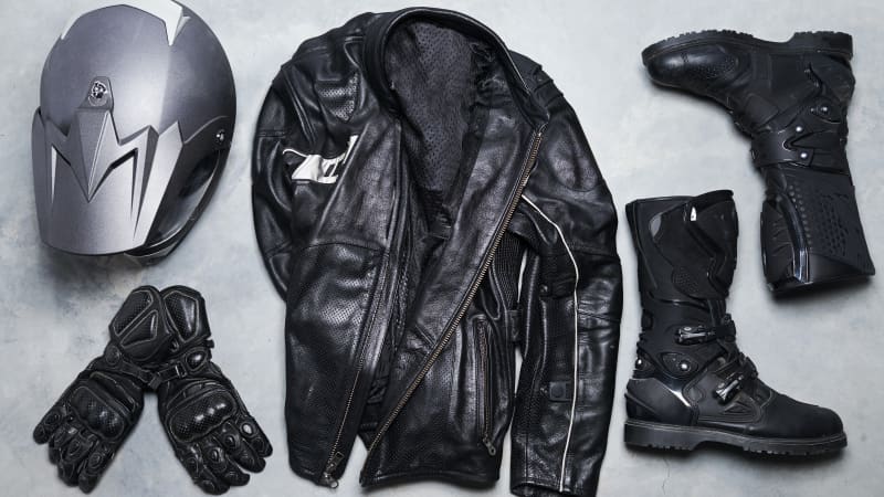 Ein Motorradhelm, Handschuhe, eine Lederjacke sowie Motorradstiefel von oben auf dem Boden