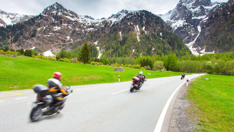 Drei Motorradfahrer auf einer Straße in den Alpen