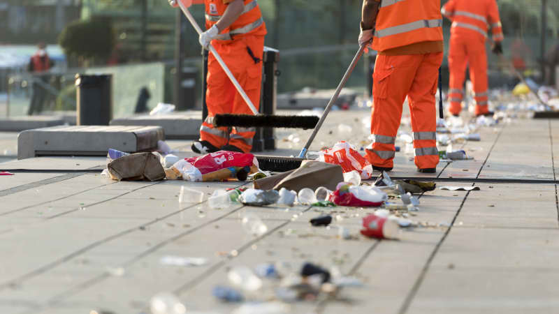 Straßenkehrer bei der Arbeit fegen Müll auf einem Platz zusammen