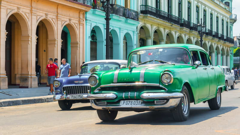 Ein grüner und ein blauer Oldtimer in einer Straße mit bunten Häusern in Havanna
