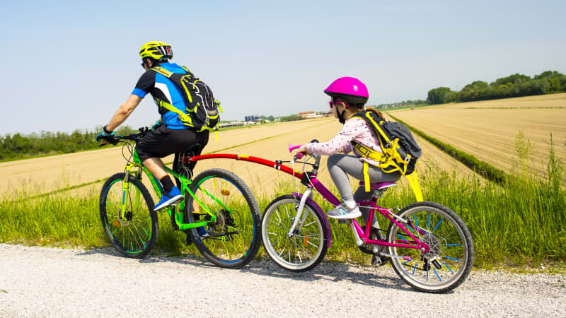 Kinderfahrrad eines Mädchen ist mit einer Tandemstange am Fahrrad des Vaters befestigt