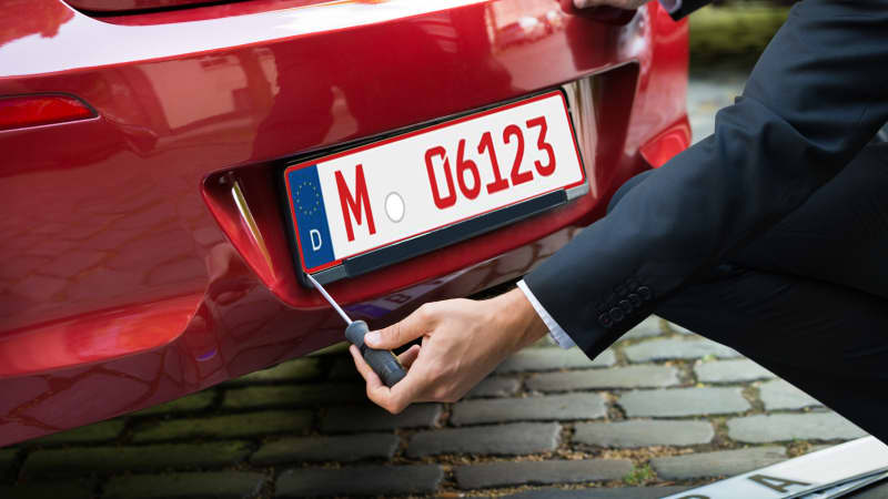 Autohändler schraubt ein rotes Nummernschild an einen Wagen