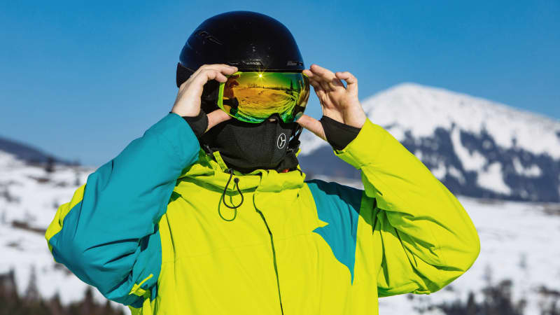 Skifahrer setzt seine Skibrille auf und trägst einen Mund-Nasen-Schutz