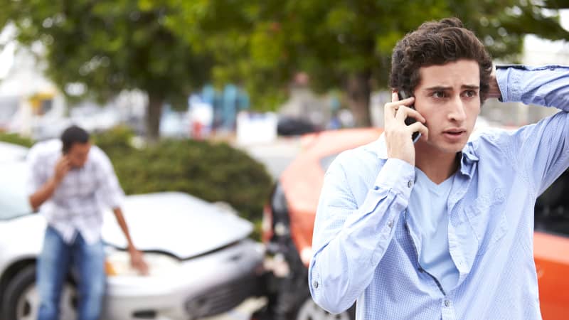 Junger Mann telefoniert nach einem Autounfall