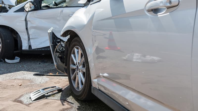 Ein weisses und silbernes Auto mit Blechschäden nach einem Unfall, Blechteile liegen am Boden
