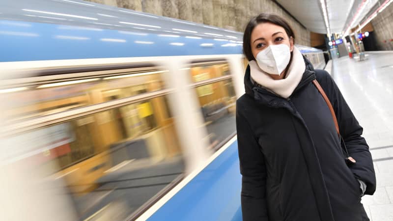 Eine U-Bahn fährt an einer Frau, die eine FFP2 Maske trägt, vorbei