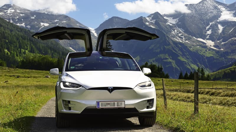 Ein Tesla Model X steht auf eine Weg vor Bergkulisse, mit geöffneten Flügeltüren