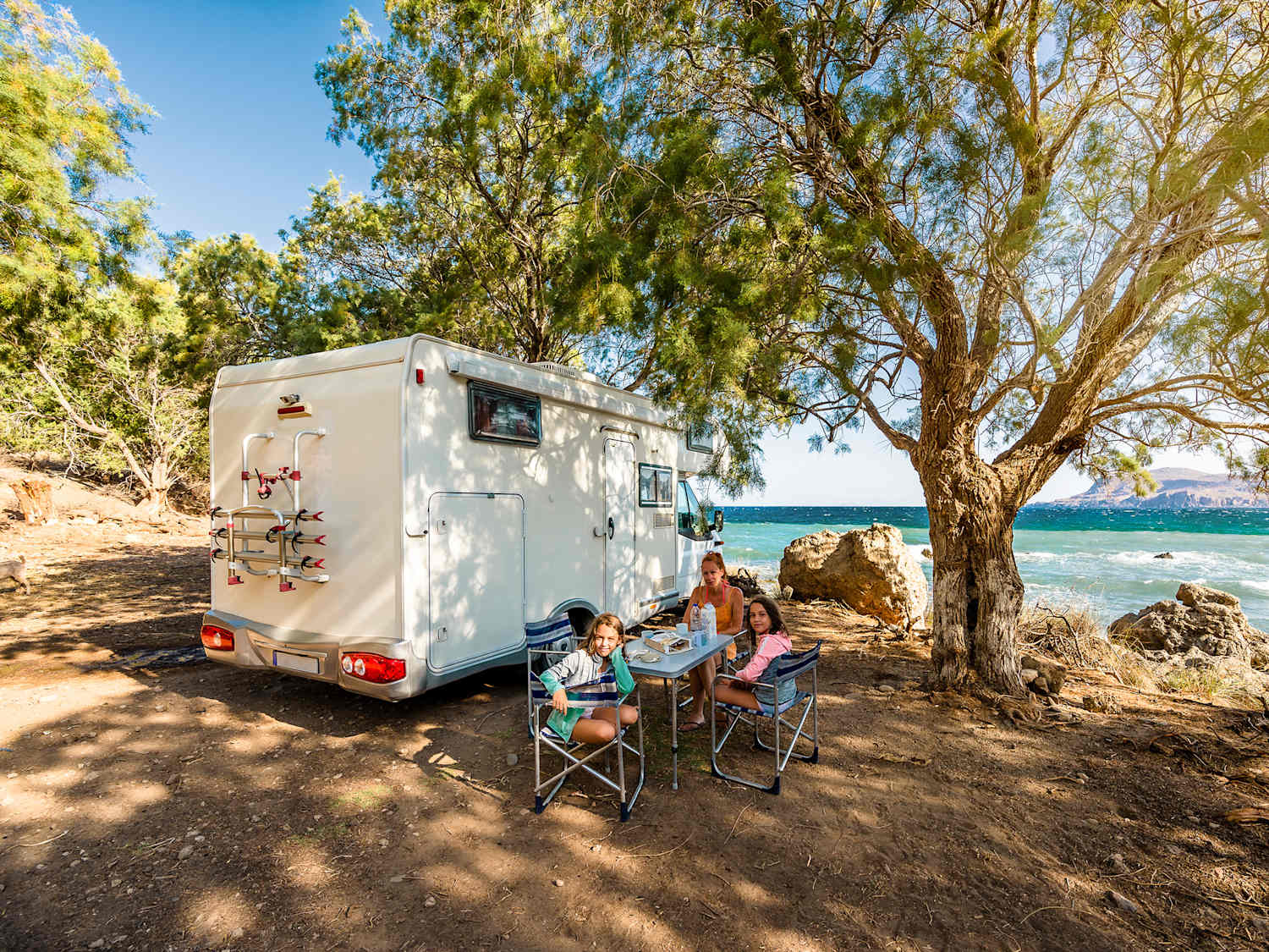 Eine Familie steht mit ihrem Wohnmobil in Griechenland mit Ausblick aufs Meer