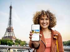 frau zeigt handy mit screen der trips app. im hintergrund sieht man den eiffelturm