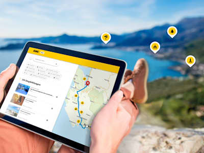 Ein Mann sitzt mit seinem tablet im Urlaub auf einem Berg