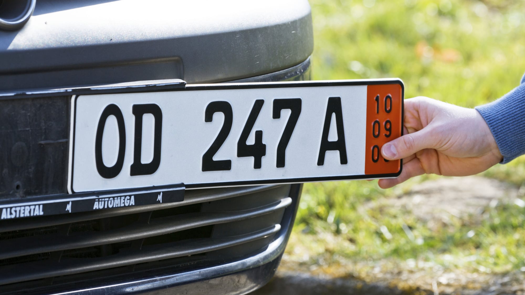 Ein Mann befestigt an der Prägestelle in Bad Oldesloe ein Ausfuhrkennzeichen an einem Auto