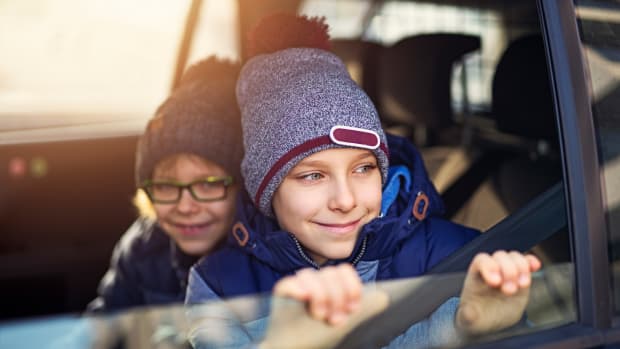 Zwei Kinder sitzen mit Winterjacke und Mütze im Auto am offenen Fenster