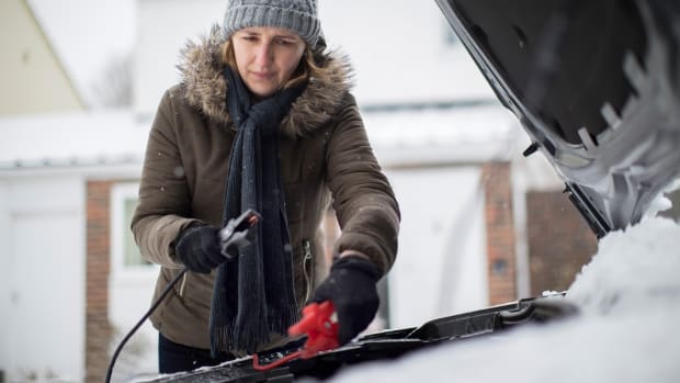 Frau im Winter gibt Starthilfe mit Überbrückungskabel