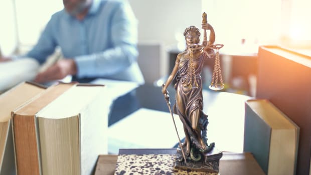 Statue Justizia auf einem Schreibtisch voller Bücher