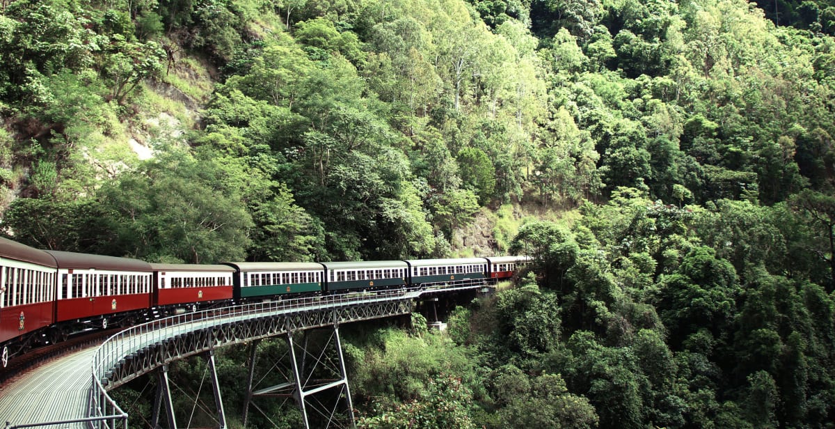 Ein Zug der Kuranda Scenic Railway fährt in Australien über eine Brück in den Dschungel