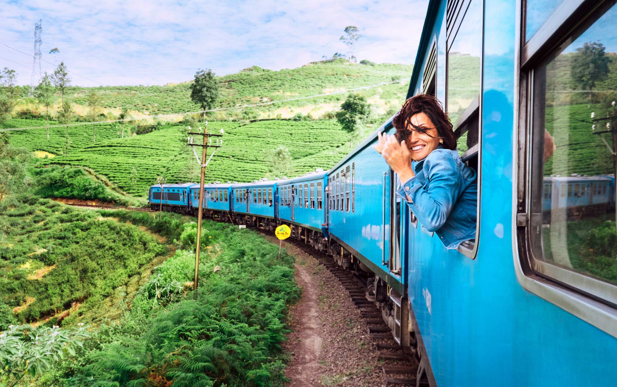 Eine Frau schaut aus dem Fenster eines fahrenden Zuges in Sri Lanka auf Teeplantagen.