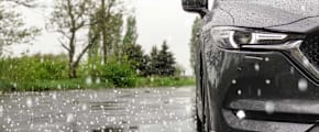 Hagelkörner prasseln auf Straße und Auto - Hagelschaden am Auto ADAC Autoversicherung