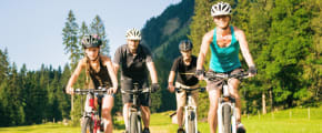 Familie fährt mit Mountainbikes über Wiese - Unfallversicherung ADAC