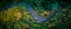 Auto fährt auf Straße durch grünen Wald - Ressourcenschonend Fahren ADAC