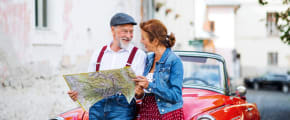 Paar schaut auf Karte vor rotem Oldtimer - Oldtimerversicherung ADAC