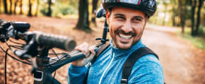 Mann schultert Mountainbike im herbstlichen Wald - Unfallversicherung ADAC