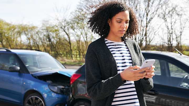 Frau meldet Kfz Schaden über Smartphone, im Hintergrund ein Auffahrunfall - Schadenmeldung Kfz ADAC
