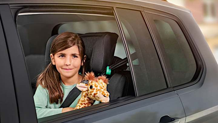 Maedchen schaut mit Plüsch-Giraffe aus dem Autofenster - Autoversicherung ADAC