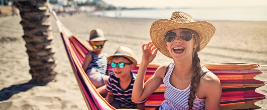 Drei Kinder sitzen in einer Hängematte an einem Strand in Spanien