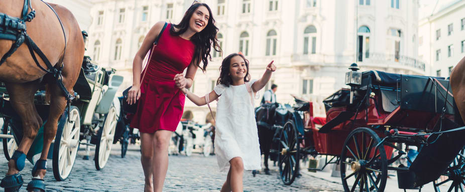 fröhliche Mutter mit kleiner Tochter in sommerlicher Kleidung vor Fiakern in Wien