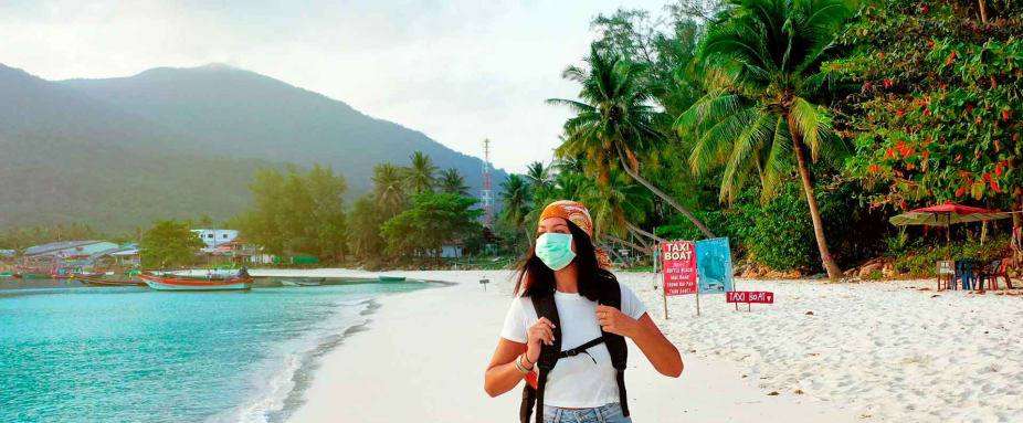 Reiseversicherung: Frau im Urlaub am Strand währen Corona