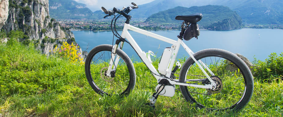 Weißes E-Bikes steht auf einem Hügel in der Wiese, im Hintergrund ein See und Berge