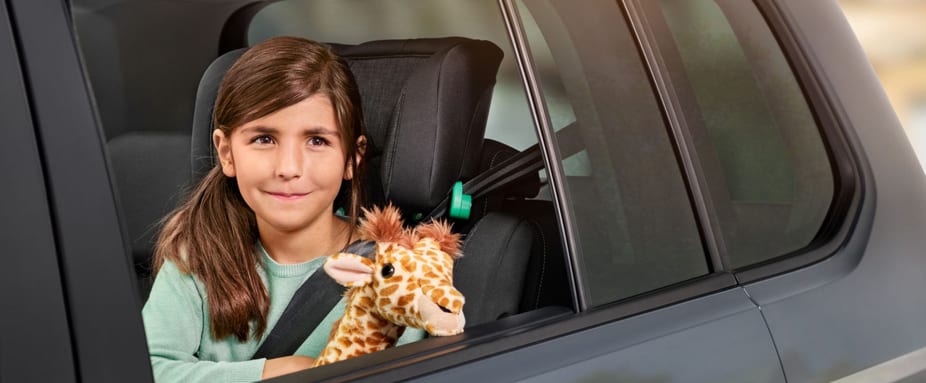 Maedchen schaut mit Plüsch-Giraffe aus dem Autofenster - Autoversicherung ADAC