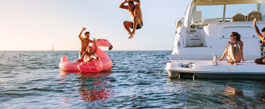 Haftpflicht im Ausland: Freunde auf Boot im Meer, Mann springt in das Wasser