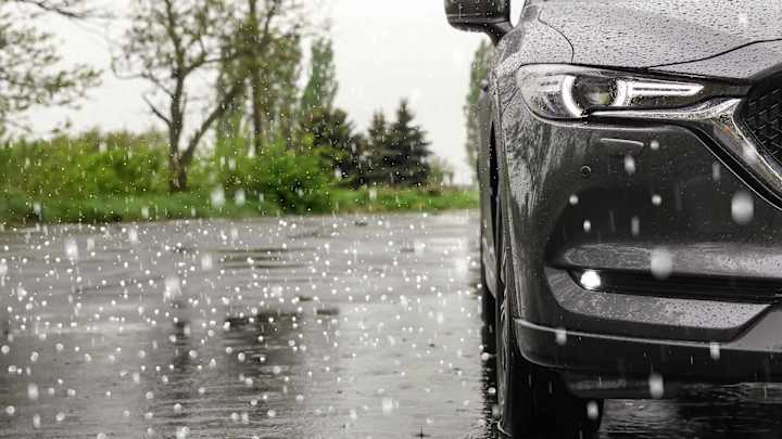 Hagelkörner prasseln auf Straße und Auto - Hagelschaden am Auto ADAC Autoversicherung