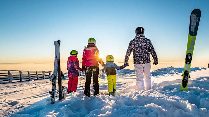 Familie steht im Schnee vor Sonnenuntergang - Unfallversicherung ADAC