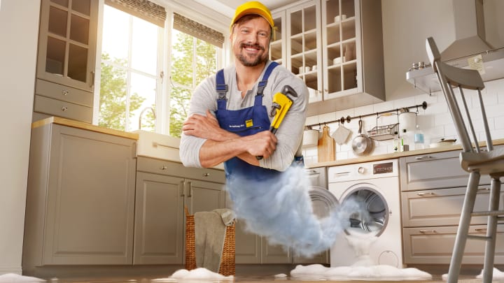 Handwerker mit Rohrzange erscheint aus Waschmaschine - ADAC Zuhause-Schutzbrief
