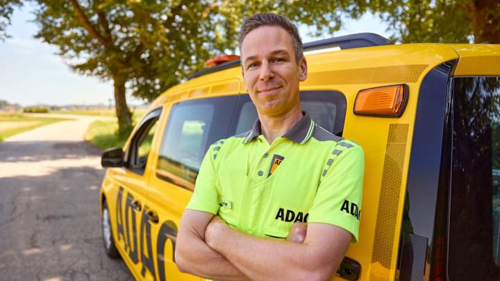 Strassenwachtfahrer steht vor dem ADAC Auto und lächelt